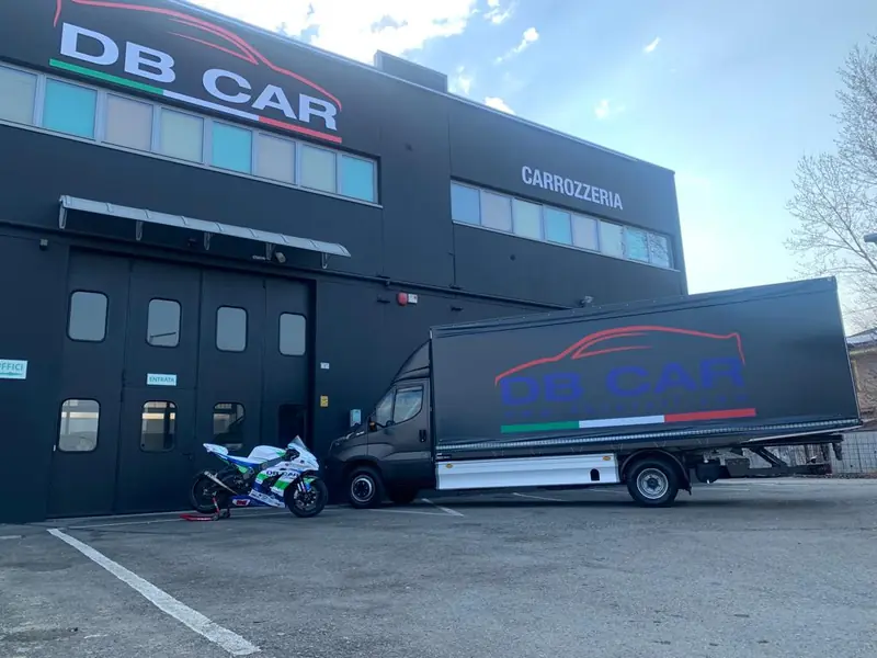 Autocarro centinato con il logo DB Car davanti all’officina